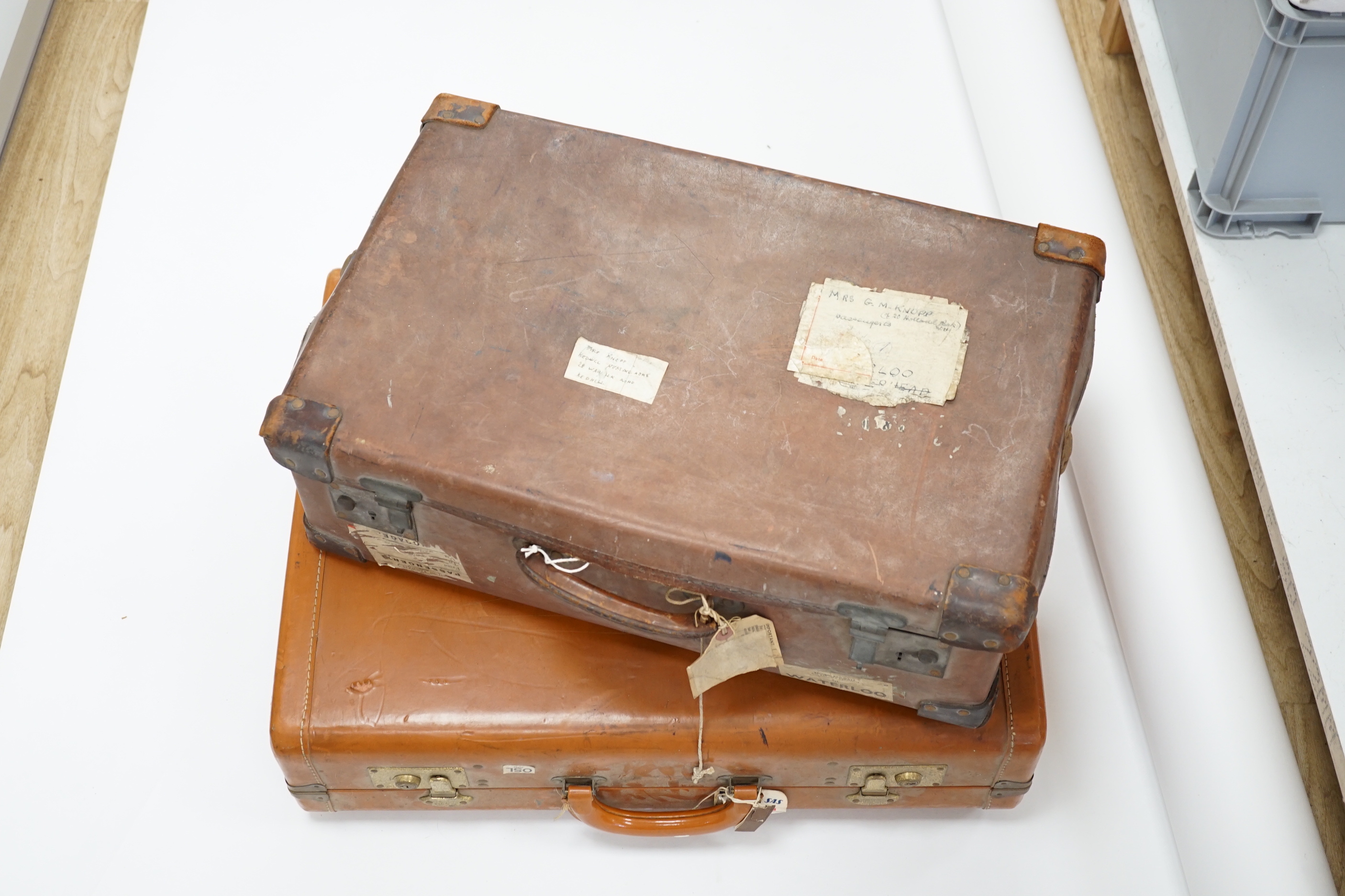 Two vintage suitcases with various labels including British Railways Waterloo, the largest 61cm wide